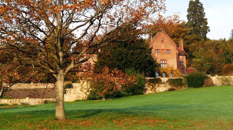 The red-brick house at Chartwell, Kent, seen across a lawn with a tree with russet leaves, and russet leaves on the ground around it, seen in October